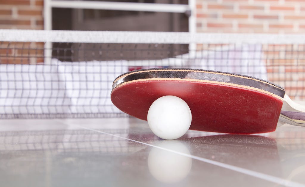 White Pingpong Ball Beneath Red Table Tennis Paddle